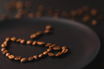 A cup of coffee. The cup on a matte black plate on a black background. Coffee beans around the plate. Black composition. Dark mode style. Coffee time. Closeup. Horizontal picture