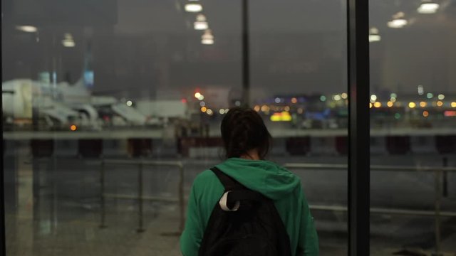 A young girl, woman waiting and taking pictures at an airport of airplanes at night. Back rear view.