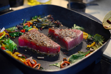 Cooking fresh tuna steaks on skillet. Sautéing vegetables. Preparing and cooking colorful food. Beautiful food preparation, chef cooking gourmet meal.