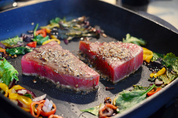 Cooking fresh tuna steaks on skillet. Sautéing vegetables. Preparing and cooking colorful food. Beautiful food preparation, chef cooking gourmet meal.