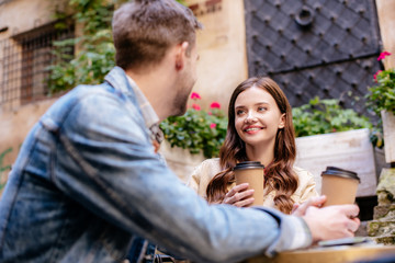 Selective focus of couple with disposable cups of coffee looking at each other in cafe in city