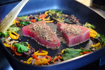 Cooking fresh tuna steaks on skillet. Sautéing vegetables. Preparing and cooking colorful food. Beautiful food preparation, chef cooking gourmet meal.