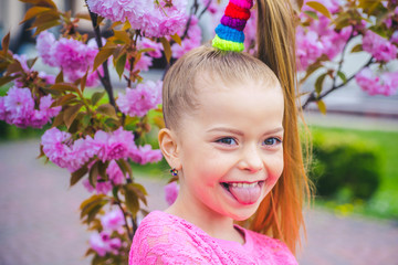 Little happy girl playing under blooming cherry tree with pink flowers. Funny face.