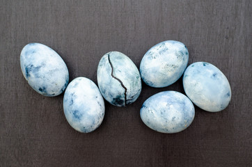 Six blue marble eggs, one of them with crack, painted in hibiscus tea, lie on black background