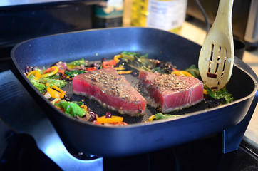 Cooking fresh tuna steaks on skillet. Sautéing vegetables. Preparing and cooking colorful food. Beautiful food preparation, chef cooking gourmet meal.