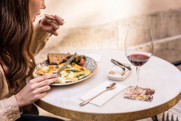 Partial view of woman eating omelette with glass of red wine in cafe