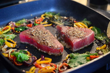 Cooking fresh tuna steaks on skillet. Sautéing vegetables. Preparing and cooking colorful food. Beautiful food preparation, chef cooking gourmet meal.