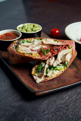 Close up view on burrito with chicken, rice, tomatoes, corn and bell pepper in brown pita on a brown plate with tomato salsa and guacamole. Vegetarian Shawarma Roll