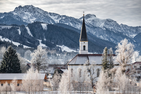 Aerial view of the small cozy german town at the mountain bottom at sunrise in a winter season, Halblech city, Germany, Bavaria, Branches of trees are covered with hoarfrost, sunny weather