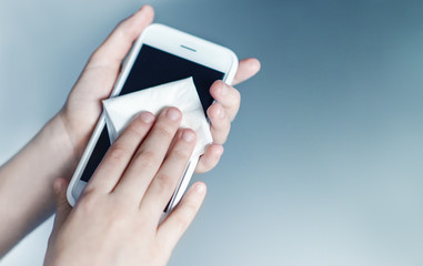 the child holds and disinfects his smartphone with a special cloth against bacteria and viruses, protection against coronavirus, close up hands on the blue background