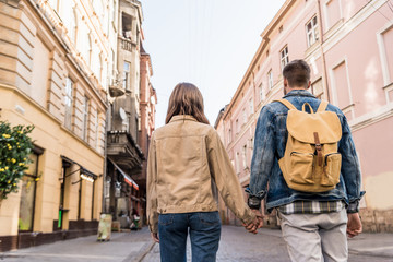 Fototapeta premium Back view of couple holding hands with backpack in city