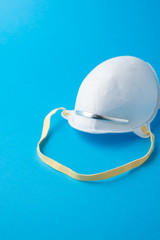 Top view of white protective mask with yellow rubber, on blue background in vertical with copy space