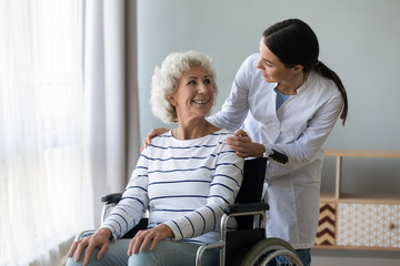 Young woman doctor give help support handicapped old lady patient sitting in wheelchair, female...