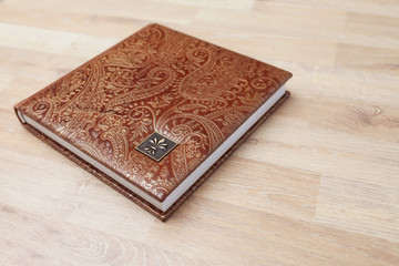 Fototapeta premium Photo book, notebook or diary with a cover of genuine leather. Brown color with decorative stamping. Wedding or family photo album. Copy space.