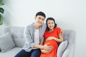 Fototapeta premium Young couple sitting on couch feeling baby kicking in mother's stomach