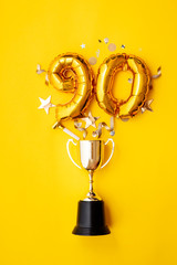 Number 90 gold anniversary celebration balloon exploding from a winning trophy