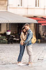 Happy couple hugging and smiling with backpack in city in Europe