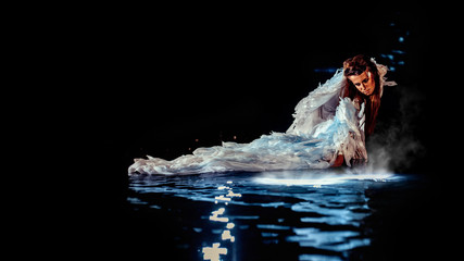 Beautiful white angel is standing in the water and looking at the underwater light.
