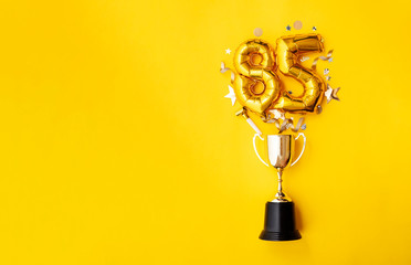 Number 85 gold anniversary celebration balloon exploding from a winning trophy