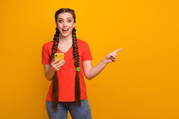 Photo of pretty funny teen lady hold telephone millennial blogger direct finger side empty space open mouth wear casual red t-shirt jeans isolated bright yellow color background