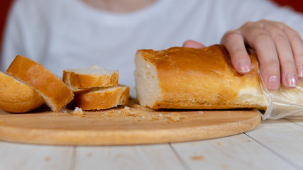 Close-up of a woman cutting bread on wooden board. Women's hands cutting baguette with big knife on chopping board.