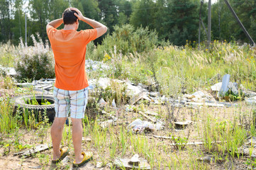 a European man stands clutching his head in terrified at a garbage dump in the forest outdoor....