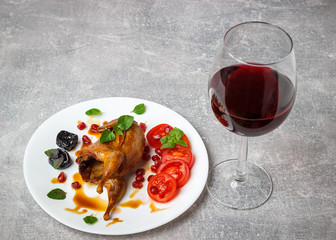 Baked quail with tomatoes, pomegranate, prunes and greens. A glass of red wine.
