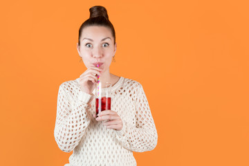 girl drinks cherry juice from straw and looks excitedly opening her eyes