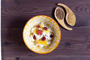Cottage cheese with sour cream, honey, strawberry, flax seeds in yellow bowl on brown wooden background