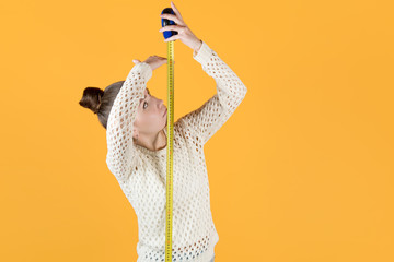 girl puzzled measures her height, holding a measuring tape nearby