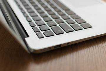 open laptop computer viewed from oblique side on wooden table · left part of the focused querty...
