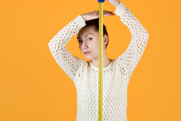 girl measures her height, holding a measuring tape nearby and looks at the camera