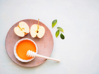 Honig in einer weißen Schüssel mit einem roten halbierten Apfel auf ienem hellgrünen Küchentisch, Flat lay, gesunde Ernärhung, Vitamin