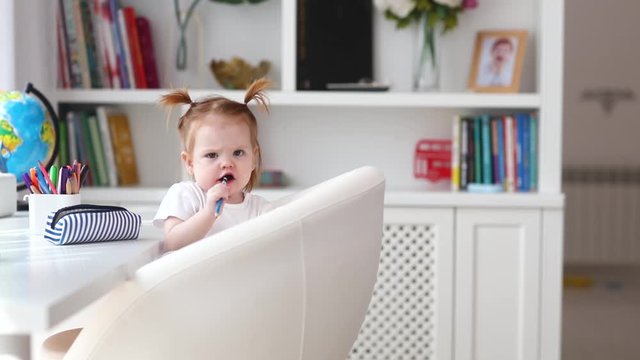 cute little baby girl biting pencil while sitting at the table at home