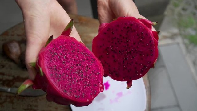 Girl cuts dragon fruit in the frame of a large hand in the background pool