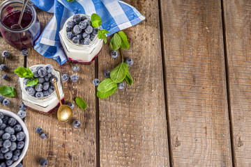 Sweet healthy yogurt with blueberry and blueberry jam in small portioned jars on wooden rustic table, copy space