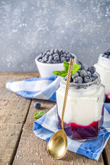 Sweet healthy yogurt with blueberry and blueberry jam in small portioned jars on wooden rustic table, copy space