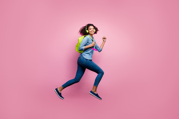 Fototapeta na wymiar Full length profile side photo of cheerful afro american girl college student jump run hurry lecture listen music headset wear denim jeans shirt bag travel isolated pink color background
