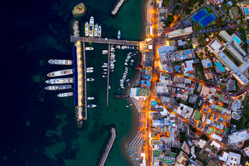 Aerial Drone top down photo of boats docked in a harbour. and street lights opened at sunset time
