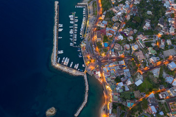 Aerial Drone top down photo of boats docked in a harbour. and street lights opened at sunset time