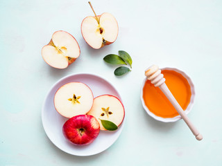 Roter halbierter Apfel auf einem Teller und eine weiße Schüssel mit Honig auf einem hellgrünen Hintergrund, Flat lay, gesunde Ernärhung