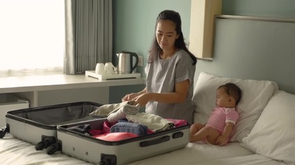cute baby sits beside the mother preparing clothes to put in the suitcase - Powered by Adobe