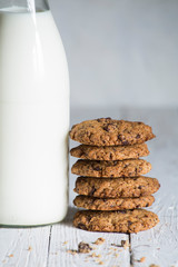 chocolate cookies stacked next to a milk bottle on top of a white wooden board, with space for text