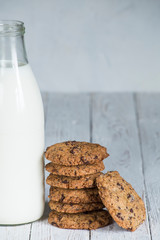 chocolate cookies stacked next to a milk bottle on top of a white wooden board, with space for text