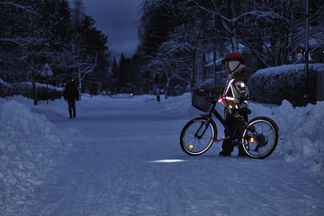 Girl on a bicycle in a winter evening. Light is reflected from clothing reflectors and bicycle wheels. Safe cycling in the dark time.