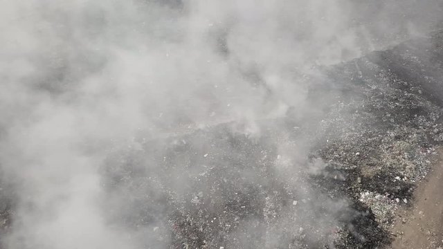 aerial sliding shot of  burning garbage at dump site : toxic smoke rising into the air	
