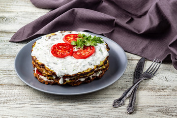Zucchini cake with tomatoes and fresh parsley on white wooden background.