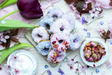 Table top scene of colorful doughnut cookies with edible flowers and birch sugar. Donut cookies. Pink and blue round raw cookies. Raw food, vegan menu. Black tulips.