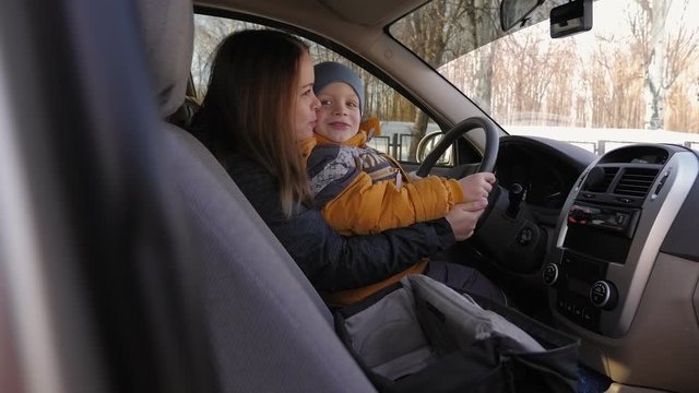 Mom And Son Are Playing In The Car In The Winter While Sitting At The Wheel Of A Car, The Boy Turns The Steering Wheel Imagining That He Is Driving. Slow Motion.