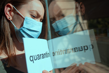 Coronavirus quarantine. A girl in a mask with the inscription Quarantine looks through the window....